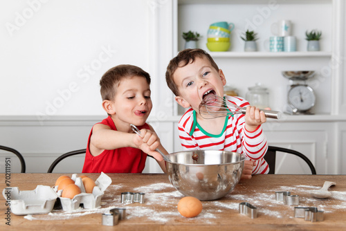 Funny siblings with messy face licking chocolate out of mixing bowl while baking photo