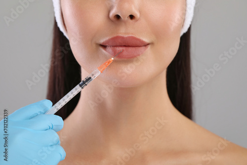 Doctor giving lips injection to young woman on light grey background  closeup. Cosmetic surgery