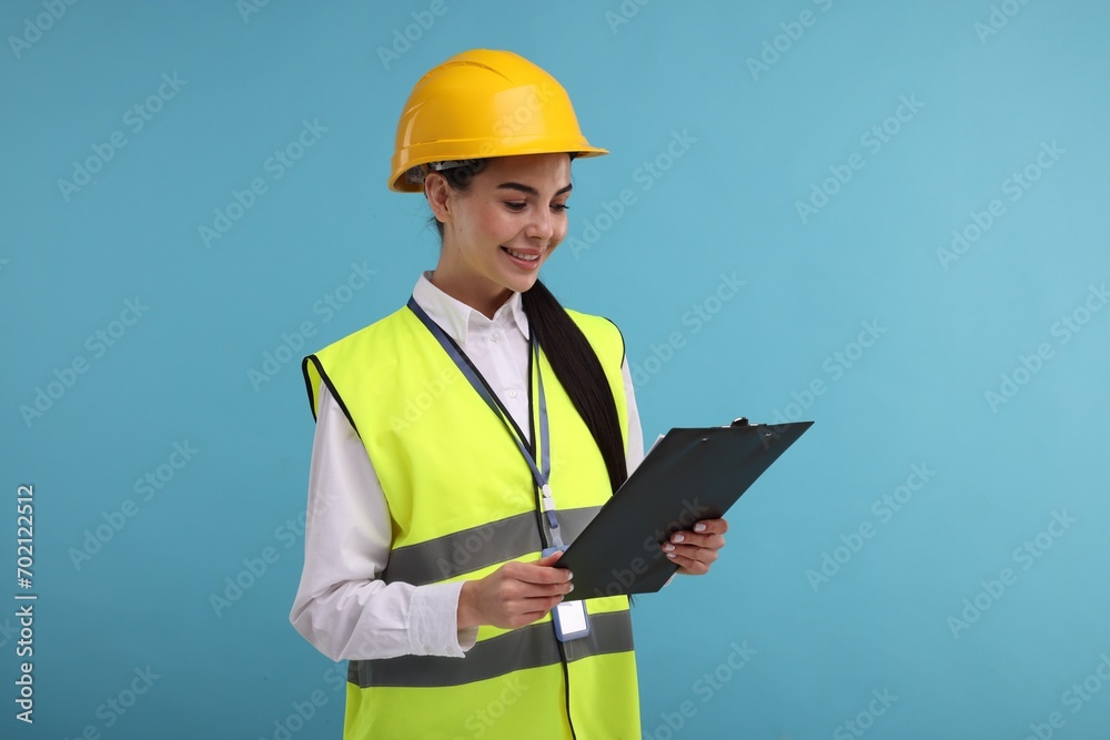 Engineer in hard hat holding clipboard on light blue background Engineer in hard hat holding clipboard on light blue background