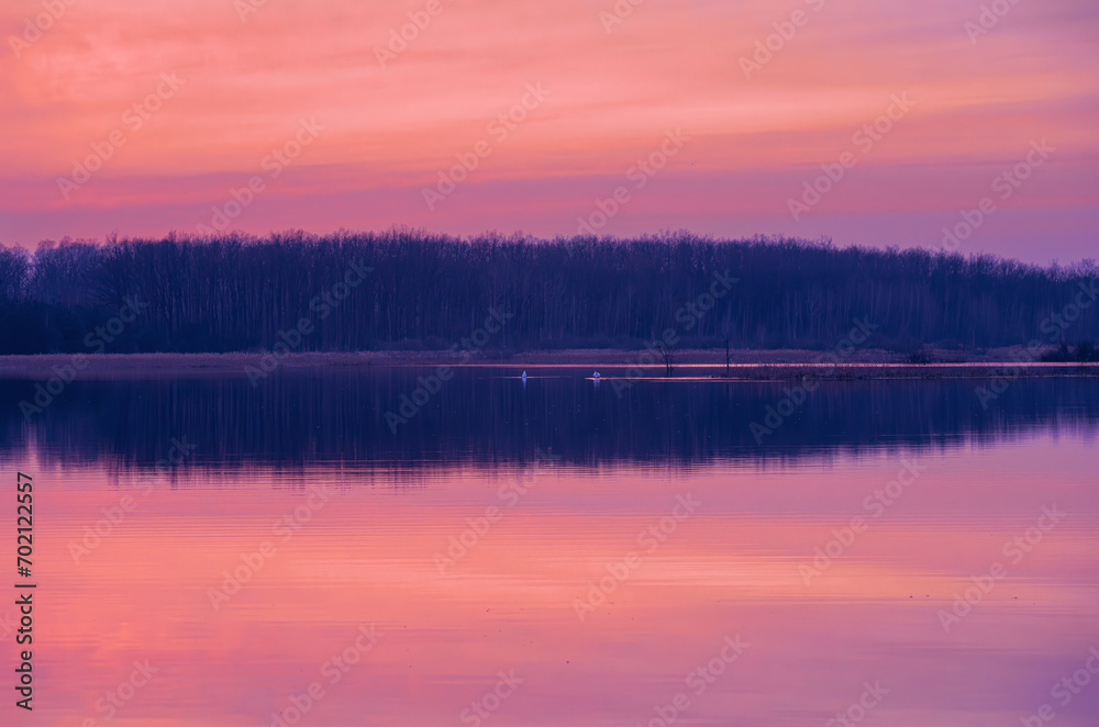 Beautiful landscape of a forest lake with the reflection of the forest in the water. Sunset in the winter season.