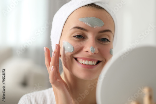 Young woman applying face mask in front of mirror indoors. Spa treatments