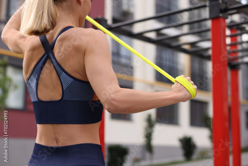 Woman doing exercise with fitness elastic band at outdoor gym, closeup photo