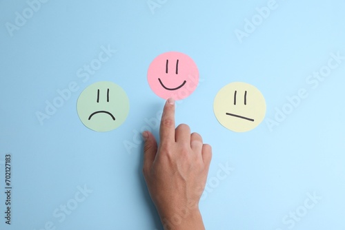 Choice concept. Woman choosing paper with happy emoticon among others on light blue background, top view