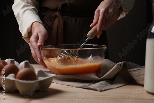 Woman whisking eggs in bowl at table, closeup photo