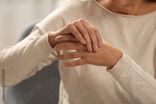 Mature woman suffering from pain in hand on blurred background, closeup. Rheumatism symptom photo