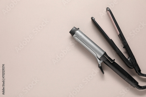 Curling iron and hair straightener on beige background, top view. Space for text