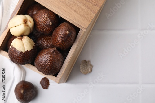 Wooden crate with fresh salak fruits on white tiled table, top view. Space for text photo