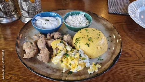 Traditional Moldovan food, meal closeup with pork stew, mamaliga polenta, fried eggs, cheese and sour cream sprinkled with parsley photo