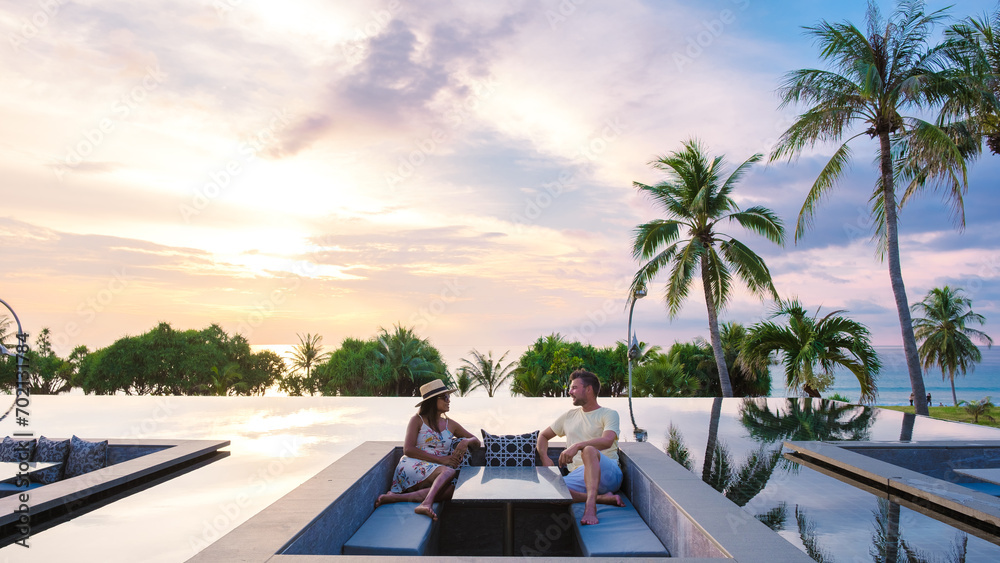 couple watching the sunset in an infinity pool on a luxury vacation in Thailand - obrazy, fototapety, plakaty 