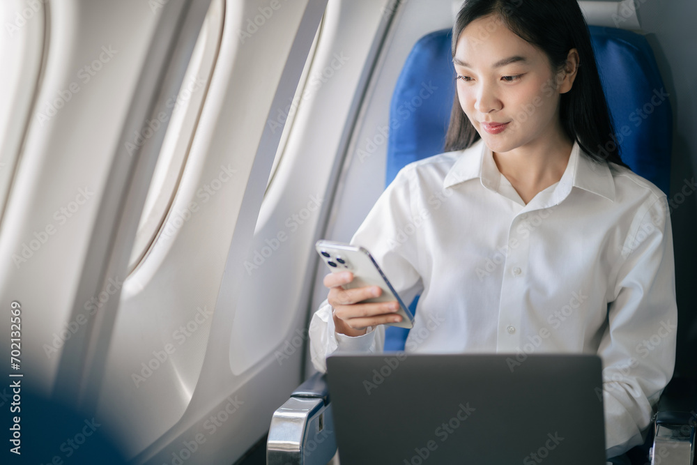 Smiling Asian woman enjoying her comfortable flight while sitting in the airplane cabin, wifi internet on the plane. Passengers near the window. Smiling Asian woman enjoying her comfortable flight while sitting in the airplane cabin, wifi internet on the plane. Passengers near the window.