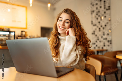 Happy woman working with laptop in cafe. A young woman freelancer in a modern coffee shop is working on a laptop. Technology concept, freelancing. Lifestyle.