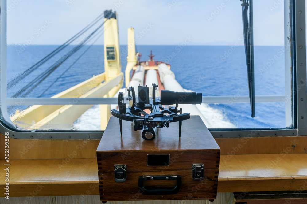 Naklejka premium Nautical black sextant placed on wooden box in navigational bridge. Navigational equipment. Celestial navigation.