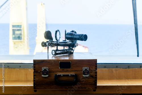 Nautical black sextant placed on wooden box in navigational bridge. Navigational equipment. Celestial navigation.