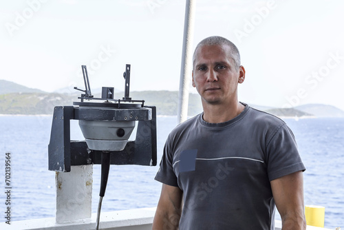Navigational officer taking bearing with azimuth ring on gyro compass on the wing of navigational bridge. Navigational equipment usage. Observations. photo