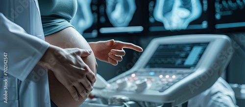 Cropped shot of a pregnant woman during ultrasound scanning at the fertility clinic Female doctor pointing at the screen of ultrasound machine Focus on ultrasound transducer on the pregnant bel photo