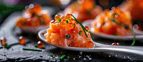 A close up on a taste of gourmet salmon tartare for catering with chives and caviar decorating on an elegant white spoon and presented on a black slate. with copy space image photo