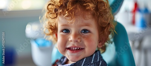 baby boy with curly red hair in blue dental chair Children s dentist. with copy space image. Place for adding text or design