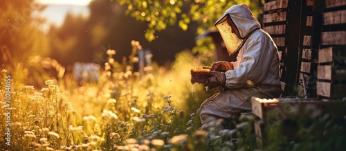 A beekeeper in a protective suit and gloves holds honey frames with honeycombs in his hands Eco apiary in nature Beekeeping Wooden beehives with bees Production and pumping of fresh honey photo