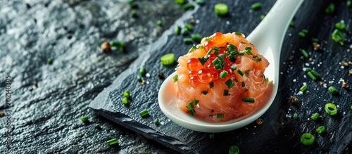 A close up on a taste of gourmet salmon tartare for catering with chives and caviar decorating on an elegant white spoon and presented on a black slate. with copy space image photo