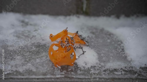 Pair of orange ice cleats drop onto pavement covered in ice. Slow motion photo