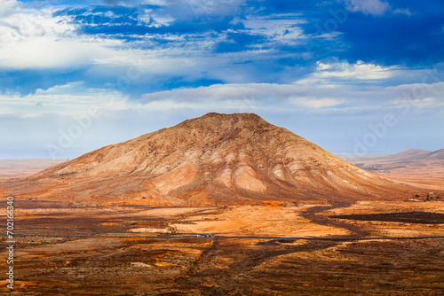 Barren desert landscape with isolated rock formations and volcanic mountains.