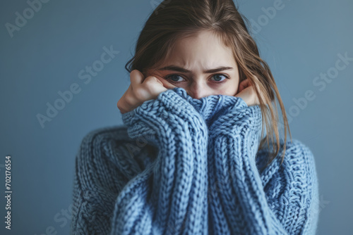 Woman in blue turtleneck knitted sweater sadly looking at camera while covering sad face. Feelings of depression, sadness, loneliness, social phobia. Winter cold. Blue Monday photo