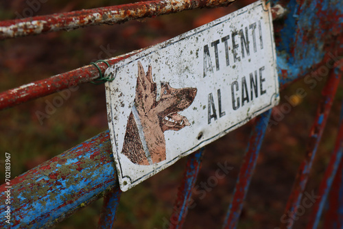 Close-up of “Attenti al cane” (italian language) Beware of Dog Sign on blue and rusty old gates
