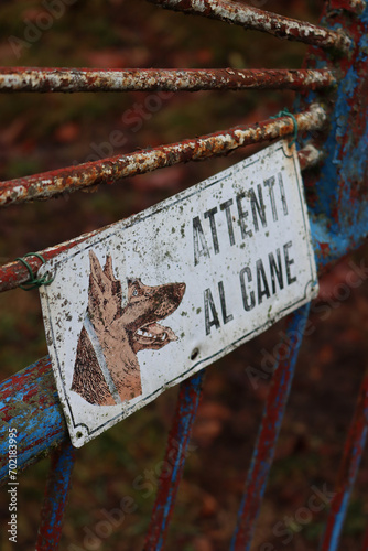 Close-up of “Attenti al cane” (italian language) Beware of Dog Sign on blue and rusty old gates