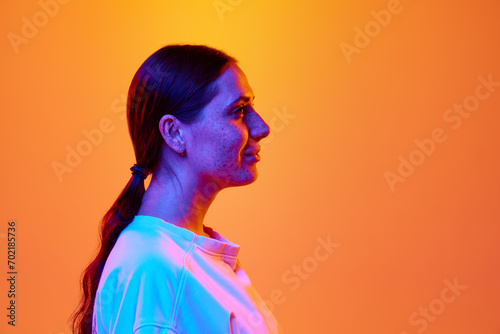 Profile view portrait of young brunette woman with long hair in tail against gradient orange-yellow background with copy space for text. Concept of beauty, youth, human emotions, self-expression. Ad © Lustre Art Group 