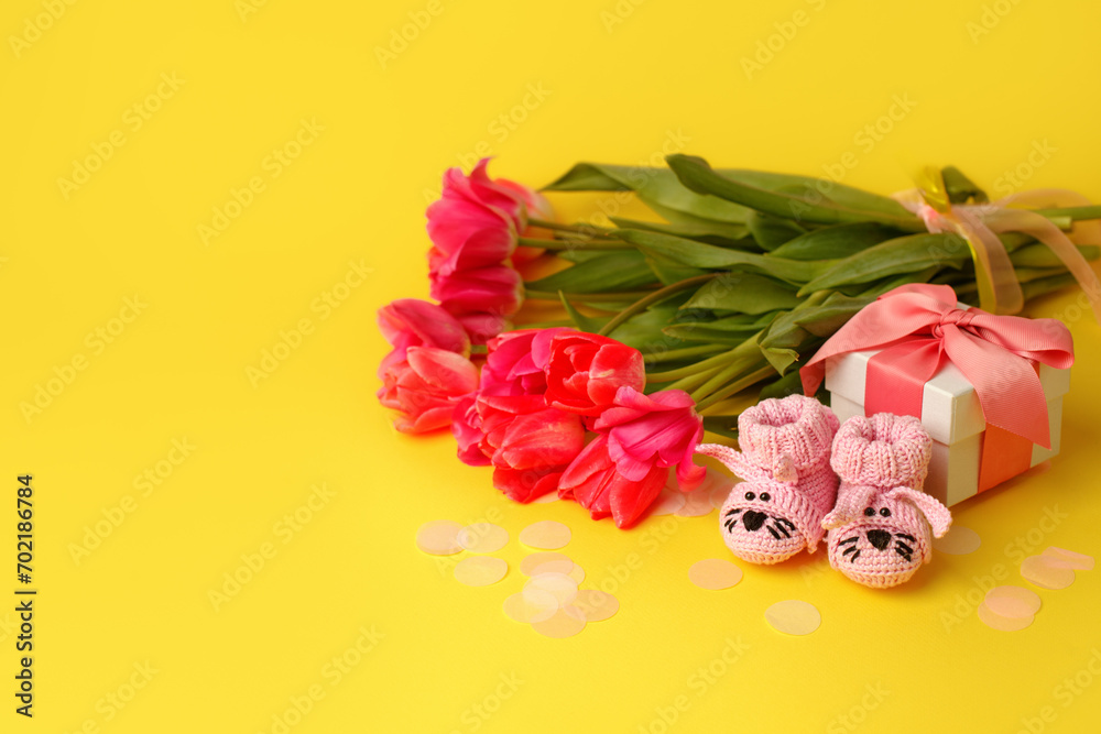 Pair of small pink baby socks, tulips and gift box on yellow background with gift present boxes and copy space for your warm message, baby shower, first newborn party background, banner Pair of small pink baby socks, tulips and gift box on yellow background with gift present boxes and copy space for your warm message, baby shower, first newborn party background, banner