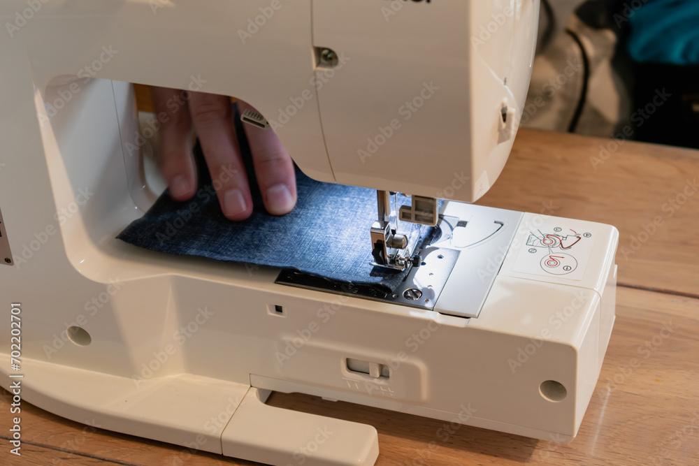 Man using a sewing machine with a blue garment, for repair work, customization, creation, upcycling