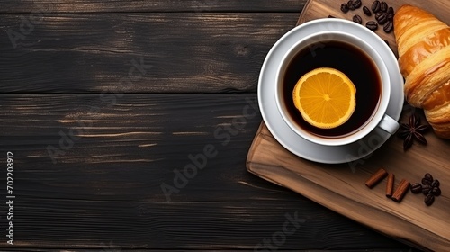 A cup of hot americano coffee with lemon and spices with fresh baked croissants on a wooden table, a warm cozy atmosphere. French breakfast. Top view, copy space background.