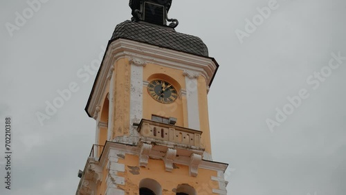 This is a close-up of an old clock tower with a weathered facade, featuring a clock face and a small bell tower against a cloudy sky, symbolizing historical architecture and the passage of time.