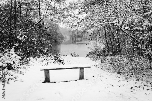 A snow covered park bench overlooking a lake on a misty winter morning.