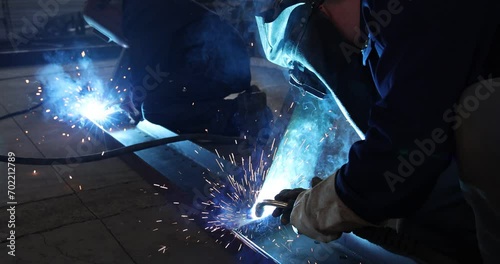 Welders at work in metal industry, welding metal construction - slow motion. Close-up shot lots of sparks in the factory photo