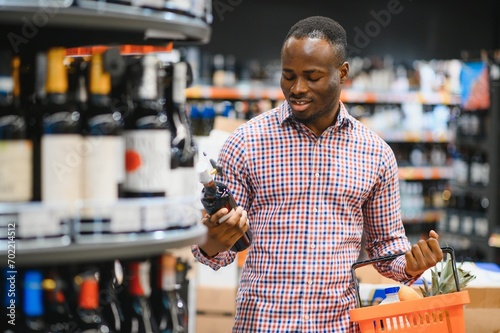 African American man holding bottle of wine and looking at it while standing in a wine store photo