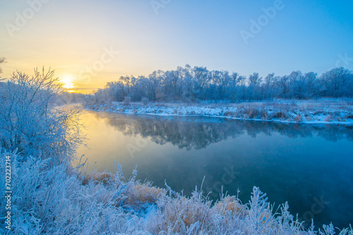 Witness a breathtaking spectacle of nature as the sun colors the sky in shades of fiery orange and pink, casting its warm glow on the icy river. Winter Magic Nature Perfection
