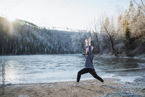 The girl is doing yoga on the smell of the rising sun in the mountains, training in the fresh air, sporing classes on the shore of the lake, winter training. photo