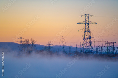 A beautiful and calm scene of a winter morning. High voltage power lines in foggy fog. Peaceful river covered with a layer of fog.