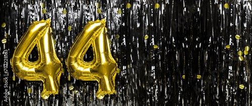 Gold foil balloon number number 44 on a background of black tinsel decoration. Birthday card, inscription forty-four. Anniversary event. Banner.