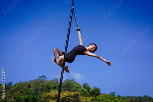 Beautiful Asian girl shows extreme advances by performing pole dance aerial in various positions and spinning stunts on the blue sky around the natural fresh and the waterfall, outdoors. photo