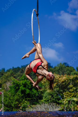 Beautiful Asian girl performing show aerial hoop or aerial ring in various positions and spinning stunts on the blue sky around the natural fresh and the waterfall, outdoors.