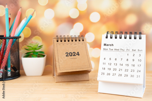White March 2024 desk calendar on wooden table with gold light bokeh background.