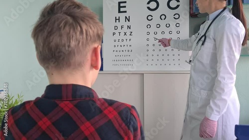 Ophthalmologist holds pen to check vision of teenage boy child. Eye test chart and vision test for adults and children photo