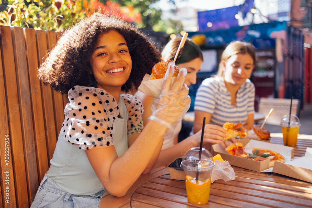Cute smiling teenage girls are sitting in open air cafe and eating fast food Cute smiling teenage girls are sitting in open air cafe and eating fast food