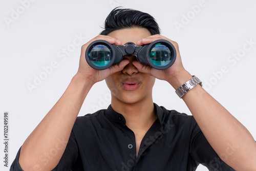 A young handsome guy looking impressed at something seen from his binoculars. Looking amazed. Wearing black polo shirt, isolated on a white background.