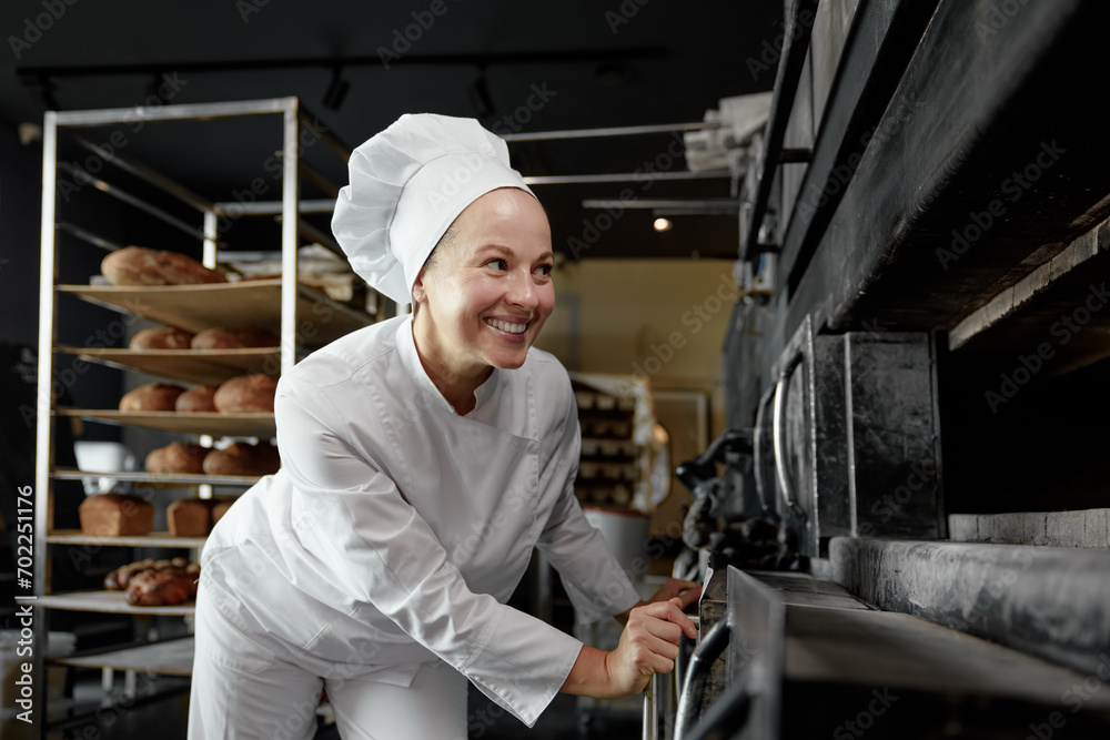 Female baker with smile on face looking at kitchen oven with bread or pastry