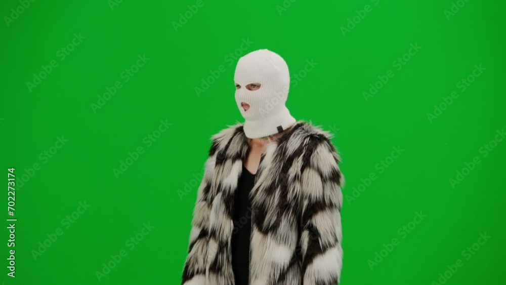Woman in white balaclava, fur coat and evening dress walking. Woman