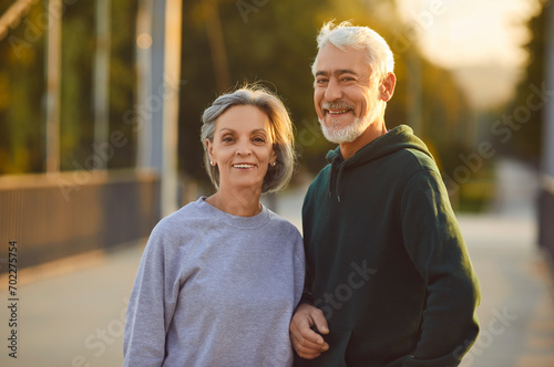 Portrait of active senior happy smiling couple family standing in city park after doing workout in nature or jogging exercises. Sport, fitness training in retirement and healthy lifestyle concept.