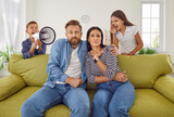 Children screaming at parents. Two naughty kids making lots of noise. Unruly brother and sister with megaphone screaming at mum and dad sitting on sofa in living room with scared face expressions